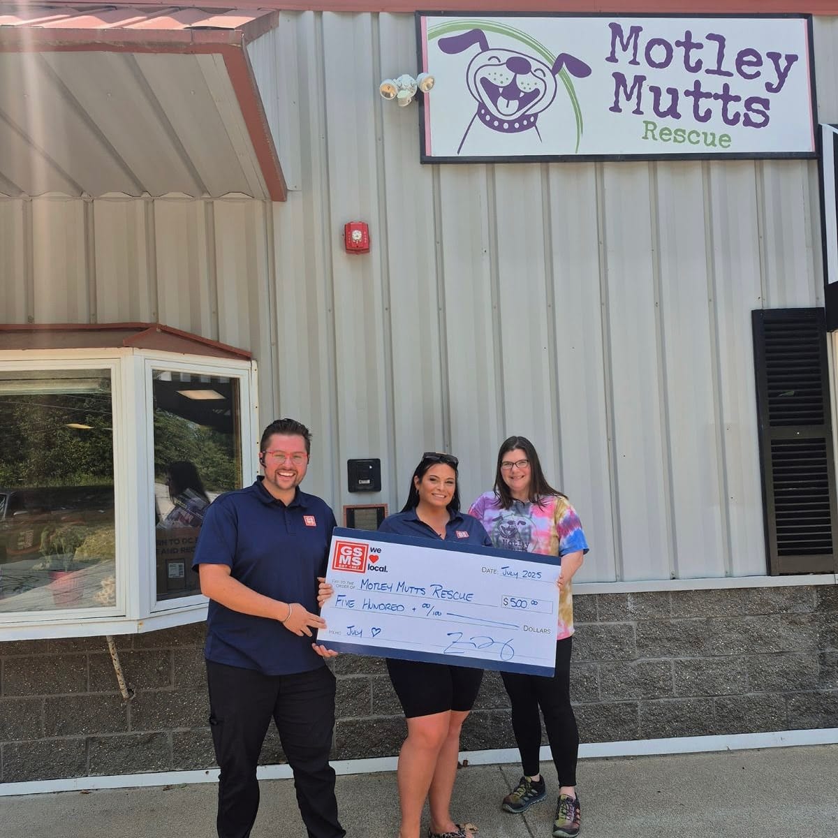 GSMS team members presenting a donation check outside the Motley Mutts Rescue facility,