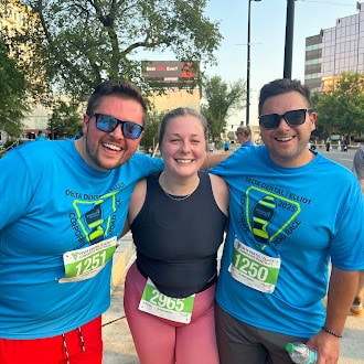 Three smiling GSMS team members in Delta Dental | Elliot Corporate 5K shirts, standing together after the race with bib numbers visible.