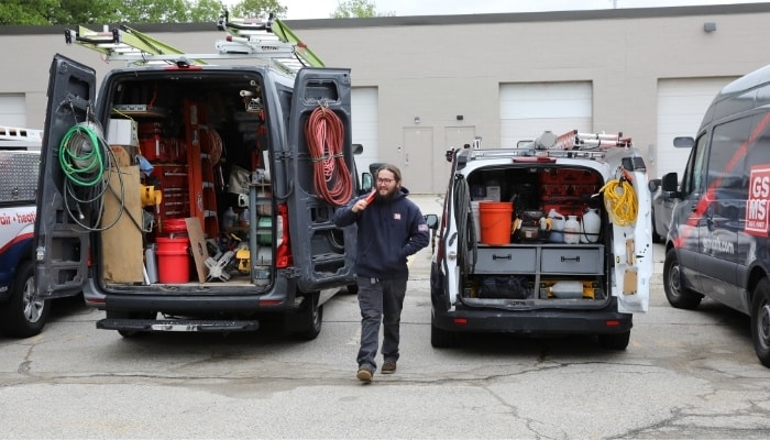 GSMS technician walking between two open service vans fully stocked with HVAC tools and equipment in Southern NH.